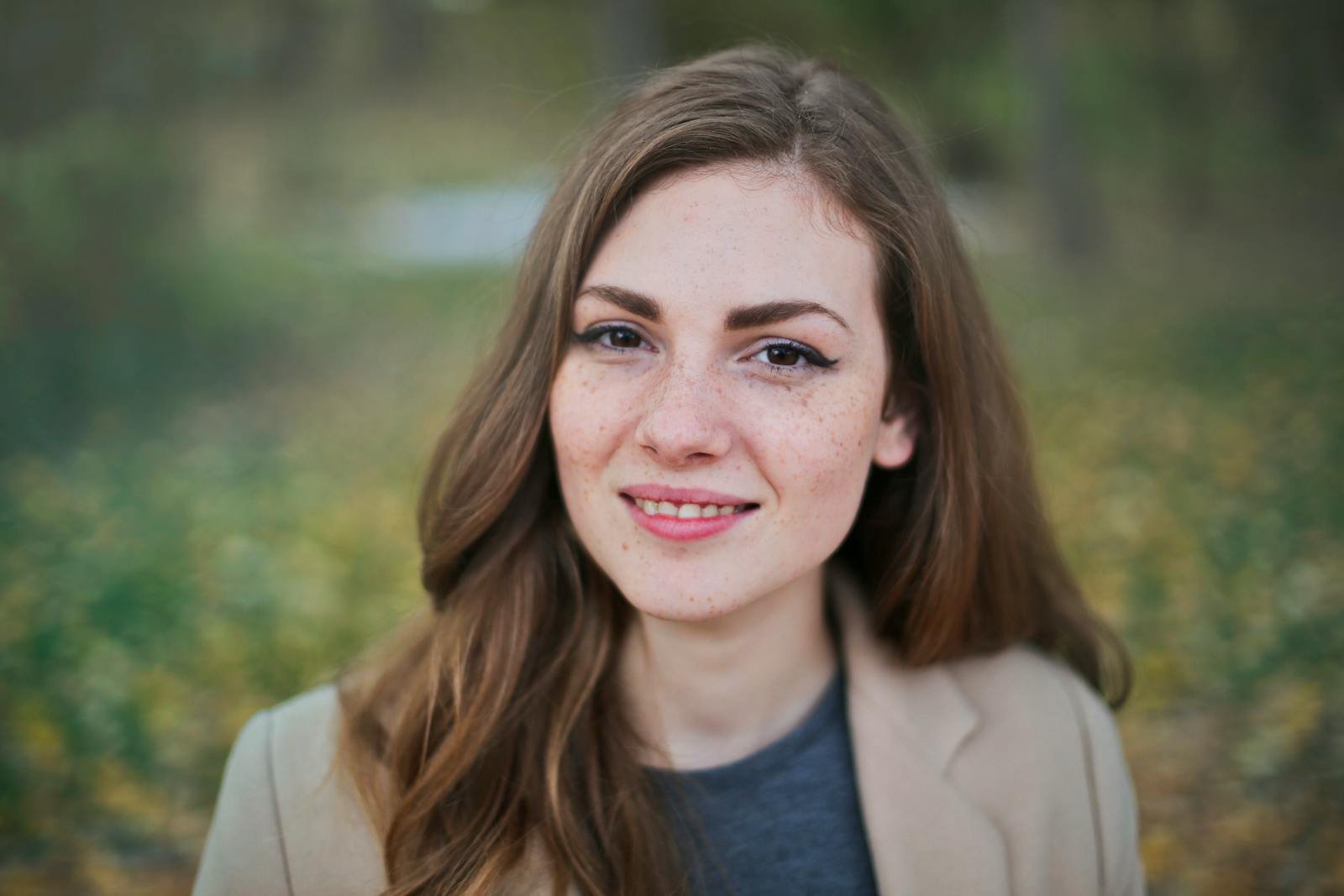 Close-up portrait of a smiling woman with freckles and long hair in a Budapest park during fall.